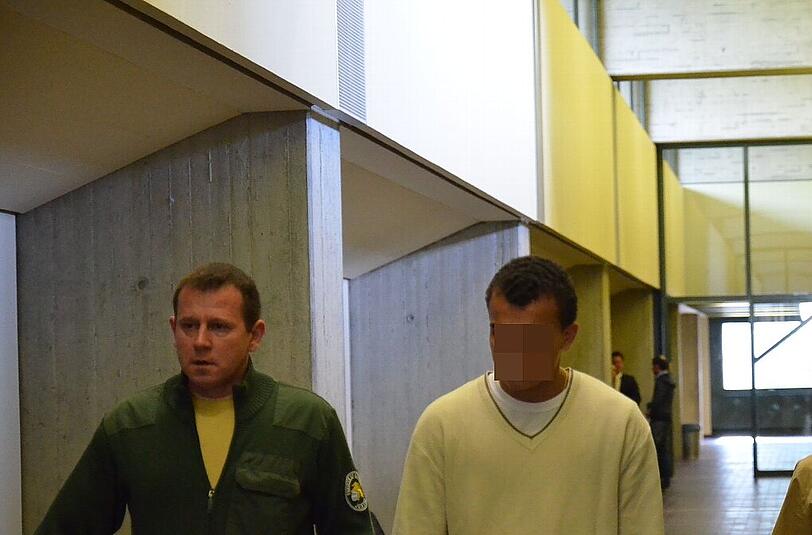Der 16-Jährige wird von einem bewaffneten Justizwachmann in Handschellen in den Landgerichtssaal 208 geführt.