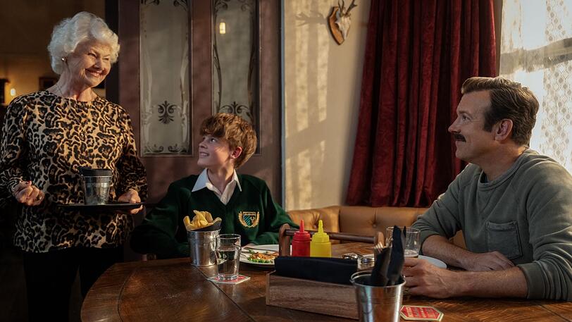 Die temperamentvolle Pub-Besitzerin Mae (Annette Badland) k&uuml;mmert sich um Ted Lasso (Jason Sudeikis) und seinem Sohn Henry (Grant Feely).