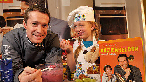 Sterne-Koch Alexander Herrmann und seine kleine Helferin Nina stellen das neue Kochbuch für Kinder vor. Und hinter dem Buch spitzt der Genuss-Sheriff hervor. Sterne-Koch Alexander Herrmann und seine kleine Helferin Nina stellen das neue Kochbuch für Kinder vor. Und hinter dem Buch spitzt der Genuss-Sheriff hervor.