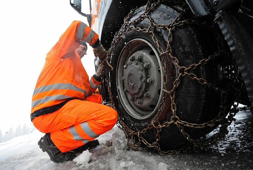 Der Mitarbeiter eines Räumdienstes bringt am Samstag auf der Straße von Schliersee nach Spitzingsee Schneeketten an seinem Fahrzeug an.