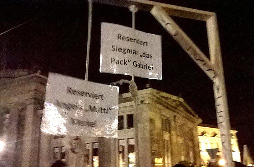Teilnehmer der Pegida Demonstration halten am 12.10.2015 in Dresden einen gebastelten Galgen hoch, an dem Schilder mit der Aufschrift "Reserviert Angela 'Mutti' Merkel" und "Reserviert Siegmar 'Das Pack' Gabriel" zu sehen sind.