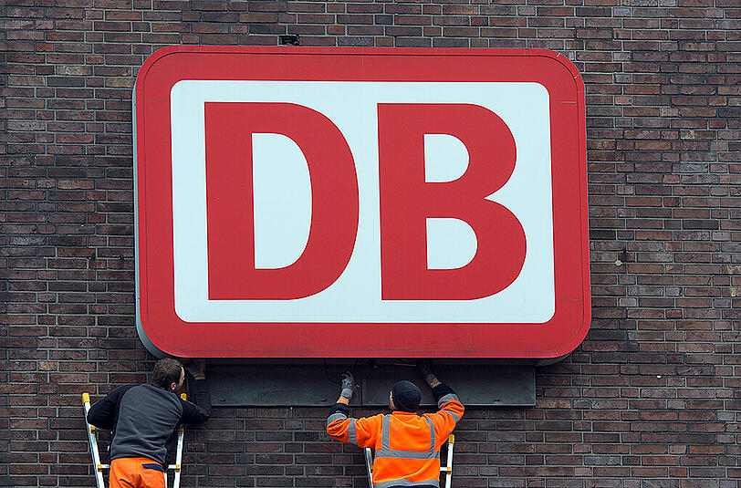Monteure arbeiten an einem Unternehmensschild der Deutschen Bahn. Foto: Federico Gambarini/Illustration