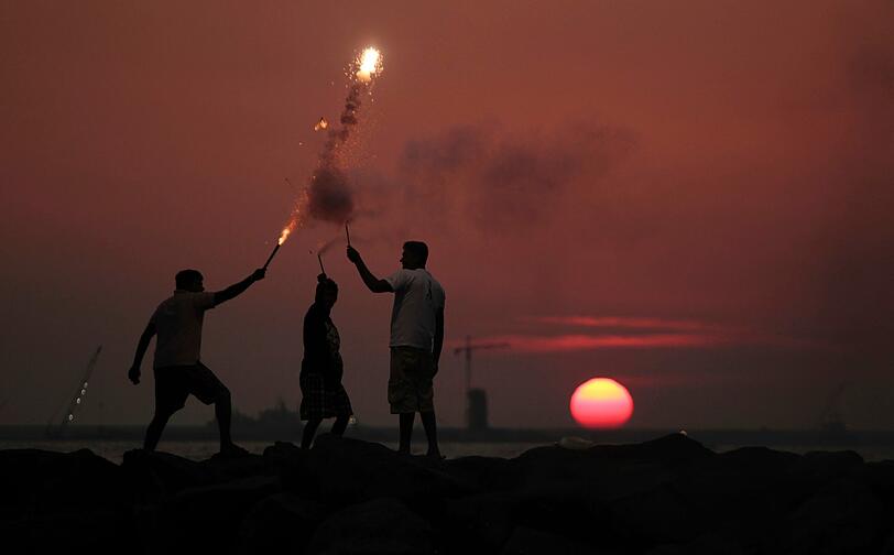 Bei Sonnenuntergang spielen Jungs mit Feuerwerkskörpern am Strand von Colombo, Sri Lanka.