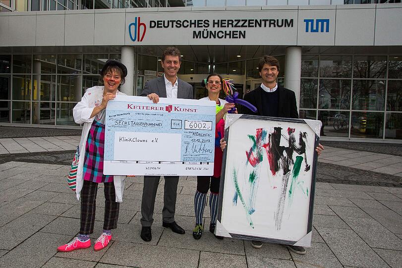Robert Ketterer und Bernd Sacher übergeben den Scheck an die gutgelaunten Klinikclowns. Daneben steht das Bild, das Mangala gemalt hat.