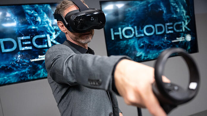 Ralf Breker, Leiter der forensischen Medientechnik beim LKA Bayern, steht mit einer VR-Brille im Tatort-Virtual-Reality-Raum.