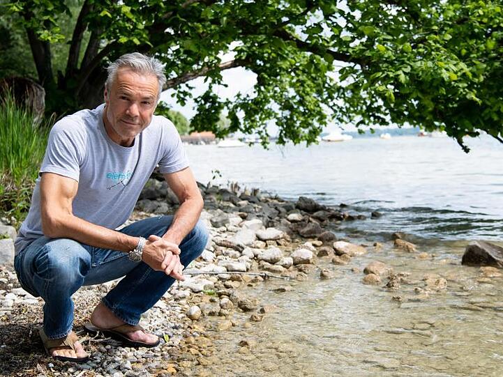 Hannes Jaenicke hockt am Ufer des Ammersees.