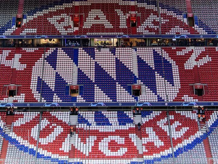 Zahlreiche farbige leere Plätze bilden in der Allianz Arena das Logo des FC Bayern München. Foto: Matthias Balk/Archivbild