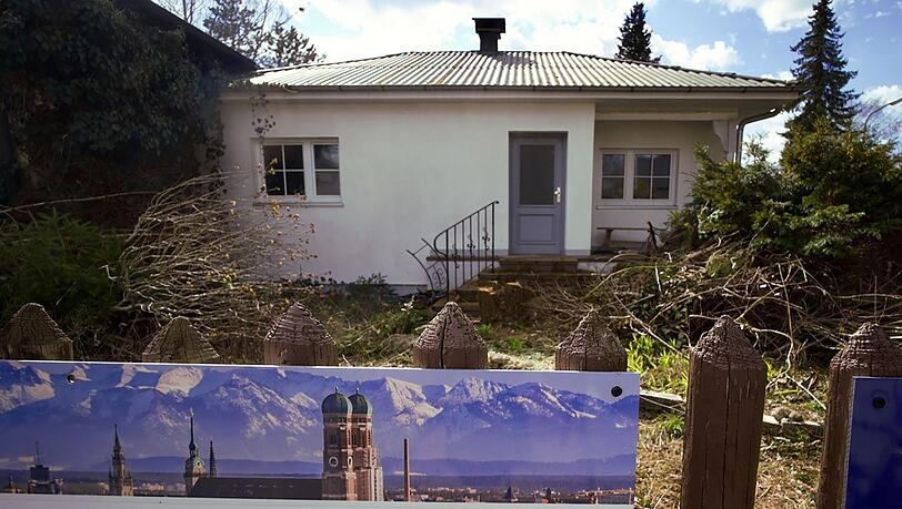 Ein zum Abriss bestimmtes Münchner Einfamilienhaus und das Werbeplakat einer Immobiliengesellschaft.