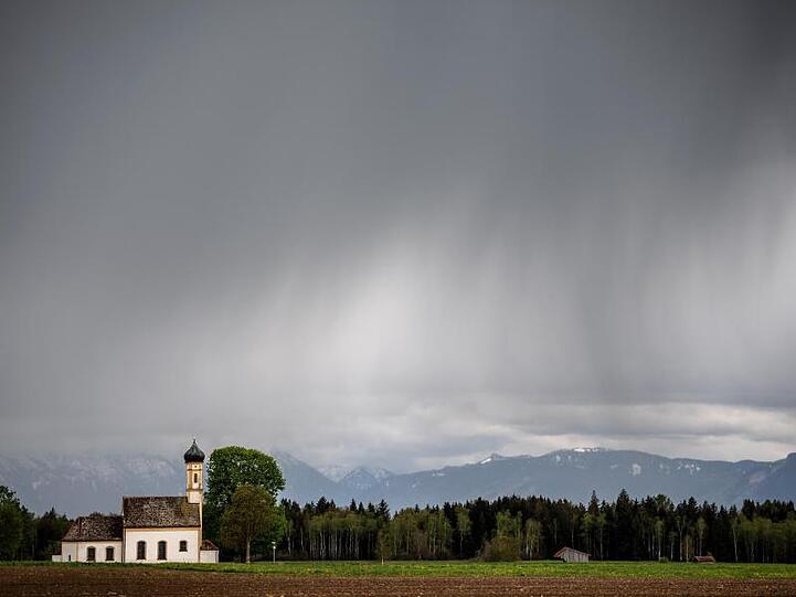 Dunkle Regenwolken ziehen über die Kirche St. Johannes der Täufer im bayrischen Rainsting.