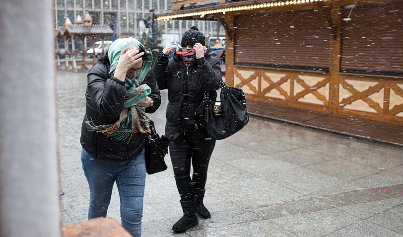 Passanten schützen ihr Gesicht bei Schneefall und starkem Wind auf dem Potsdamer Platz in Berlin.