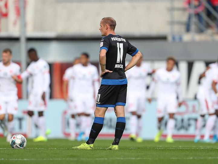 Paderborns Sven Michel zeigt sich enttäuscht nach dem Gegentreffer zum 0:1, während im Hintergrund das Mainzer Team jubelt.