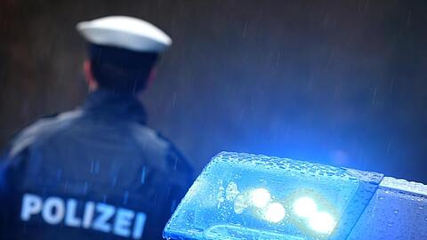 Ein Polizist steht im Regen vor einem Streifenwagen dessen Blaulicht aktiviert ist.