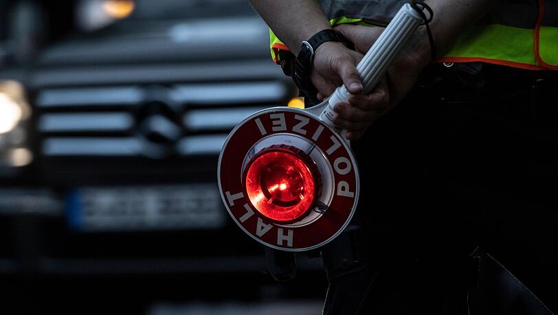 Ein Polizist hält bei einer Verkehrskontrolle eine Winkerkelle in der Hand.