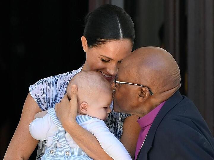 Der kleine Archie wird von Desmond Tutu mit einem Kuss begrüßt. Und Meghan strahlt über das ganze Gesicht.