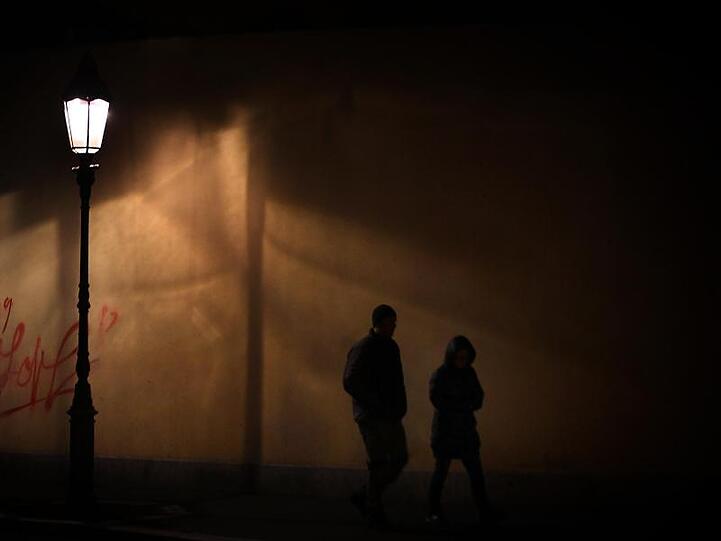 Ein Mann und eine Frau gehen zu nächtlicher Stunde im Licht einer Straßenlaterne auf dem Gehweg. Foto: Hildenbrand/Archivbild