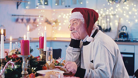 Ein Mann schaut betrübt in die Ferne und isst am 24. Dezember allein zu Abend. Zu den Feiertagen hat er es sich trotzdem gemütlich gemacht und ein großes Essen aufgetischt.