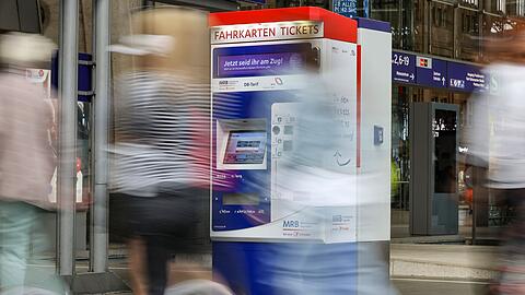 Passagiere gehen an einem Bahnhof an Fahrkartenautomaten vorbei.