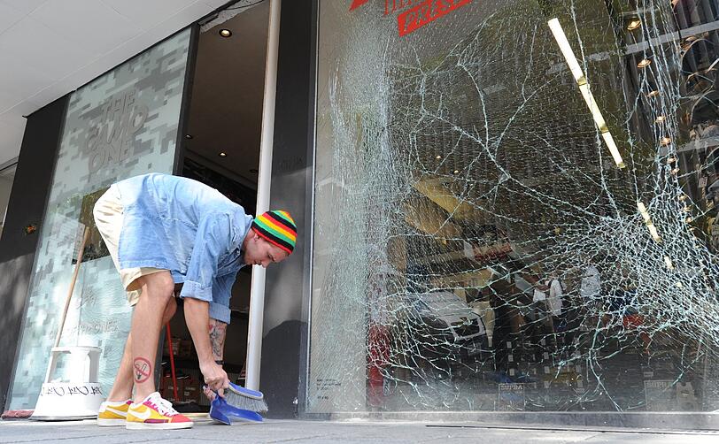 Noch ein Schaufenster in Splittern. Mit Schaufel und Besen versucht dieser Mann, sich durch die Verwüstung zu kämpfen.