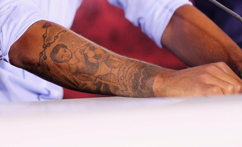 Thiago hat ein Foto seiner selbst im Alter von 14 Monaten auf den Arm übertragen, Thiago in Windeln mit einem Fußball, dazu einen Kinderwagen, ein göttliches Auge und einen Rosenkranz.