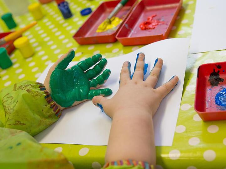 Ein Kind spielt mit Fingerfarben im Kindergarten der Katholischen Kirchengemeinde Heilig-Geist in Würzburg (Bayern). Foto: Daniel Karmann/Archiv