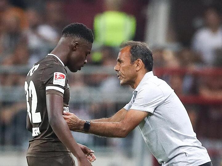 St. Paulis Trainer Jos Luhukay spricht mit Christian Conteh (l) am Spielfeldrand. Foto: Christian Charisius/dpa