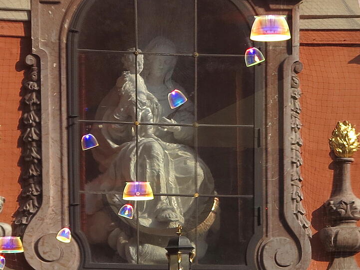 Eine Madonna mit Christkind und eine ziemlich wirr installierte Halogen-Lichterkette habe ich als Spiegelung in der Fußgängerzone entdeckt. Es spiegelt sich die Bürgersaal-Kirche im Schaufenster von Swarowski.