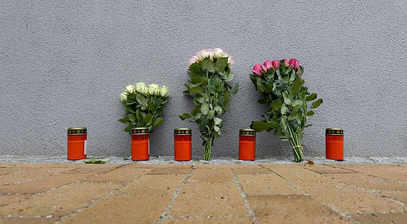 Blumen und Grablichter stehen an einem Mehrfamilienhaus. In dem Gebäude ist am Montag eine 17-Jährige nach Messerstichen gestorben. Bei dem Tatverdächtigen im Fall des gewaltsamen Todes einer 17-Jährigen in Flensburg handelt es sich um einen Asylbewerber aus Afghanistan.