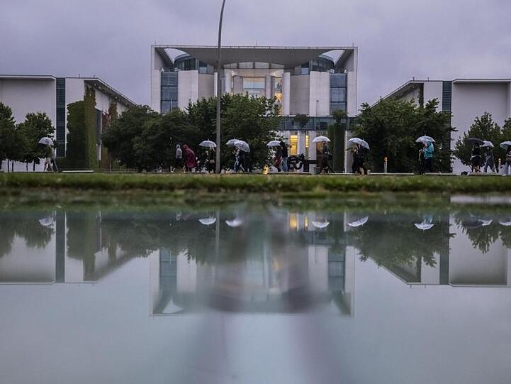 Kühl und grau: Eine Gruppe mit Regenschirmen geht am Bundeskanzleramt vorbei.