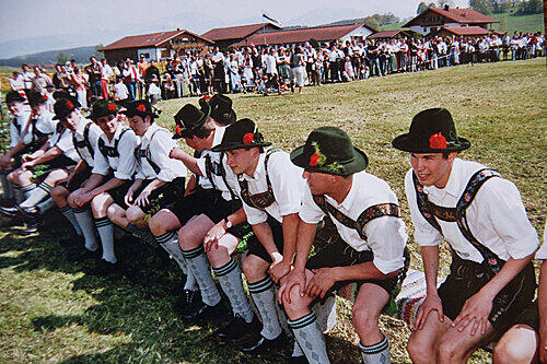 Männer gehen in Lederhose, Trachtenhut und weißem Hemd.