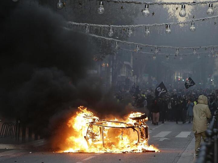 Demonstranten stehen während der Proteste in Marseille hinter einem brennenden Auto.