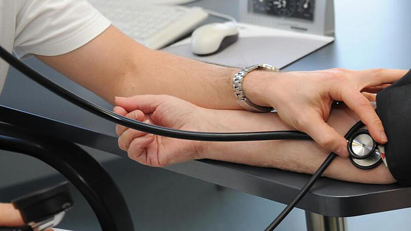 Ein Hausarzt misst bei einer Patientin den Blutdruck.