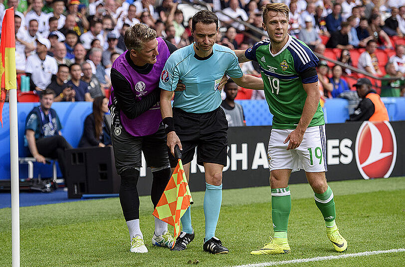 Bastian Schweinsteiger und Nordirlands Jamie Ward (rechts) helfen dem französischen Schiedsrichter-Assistenten Fréderic Cano (Mitte) auf die Beine.