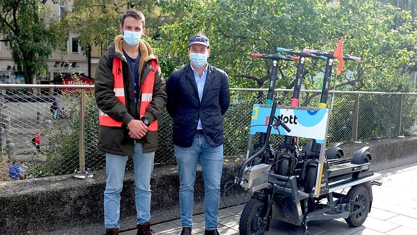 Jorge Diaz (links) und Konstantin Burger von Dott neben dem elektrischen Fahrrad-Anhänger, mit dem sie die Roller in der Stadt transportieren.
