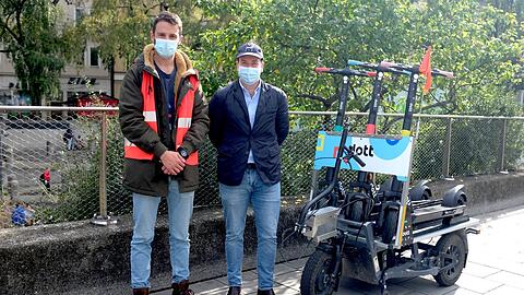 Jorge Diaz (links) und Konstantin Burger von Dott neben dem elektrischen Fahrrad-Anhänger, mit dem sie die Roller in der Stadt transportieren.