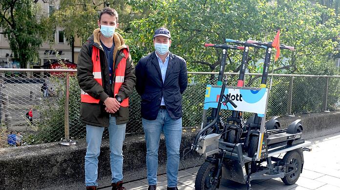 Jorge Diaz (links) und Konstantin Burger von Dott neben dem elektrischen Fahrrad-Anhänger, mit dem sie die Roller in der Stadt transportieren.