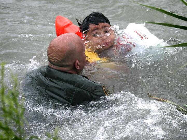 Ein US-Grenzschutzbeamter hilft einem Jungen aus Honduras, nachdem er von einem Floß in den Grenzfluss Rio Grande gefallen ist. Jedes Jahr fliehen Hunderttausende Menschen vor Gewalt und Armut in Mittelamerika.