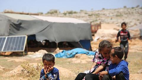 Geflüchtete Kinder sitzen in einem Flüchtlingslager nordwestlich von Aleppo auf einem Stein.
