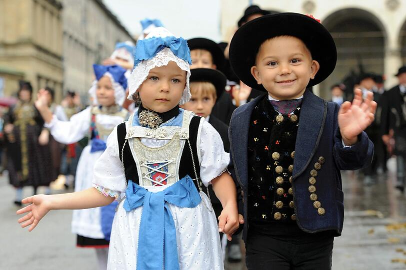 Trachtenkinder winken fröhlich in die Kamera. Sie haben Spaß und lassen sich vom Regen nicht ärgern.