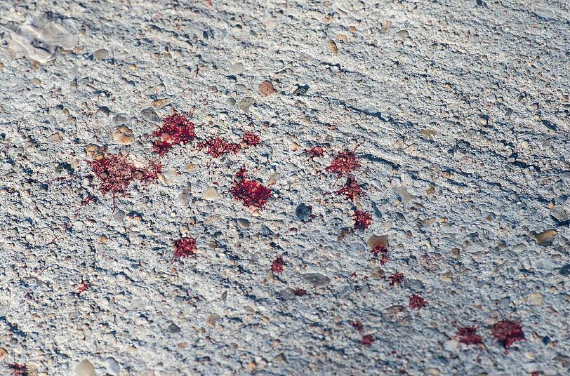 Bluttropfen auf einer Betonstraße am Tatort in Ludwigsfelde. Ein junger Flüchtling kam an diesem Ort bei einer Messerattacke ums Leben.