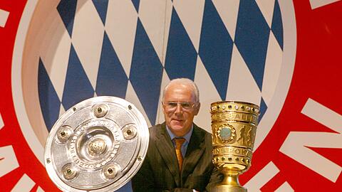Der damalige FCB-Präsident, Franz Beckenbauer, steht zwischen Meisterschale und DFB-Pokal.