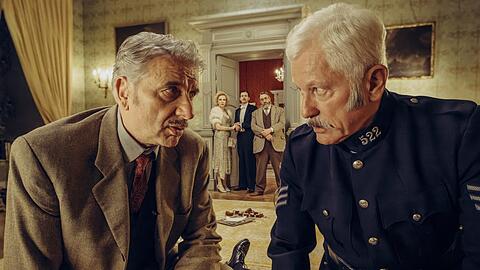 Chief Inspector Francis Lightmyer (Udo Wachtveitl, links) und Constable Ivor Partridge (Miroslav Nemec, rechts) untersuchen den toten Butler im Kaminzimmer. Lady Bantam (Sunnyi Melles), Charles (Ferdinand Hofer) und Dr. Mallard (Alexander Hörbe) beobachten sie.