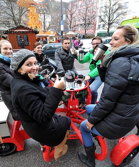 Feierfreunde prosten sich zu und fahren auf einem Glühweinbike durch München