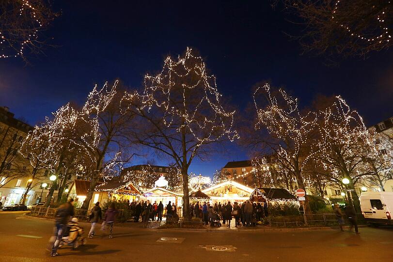 Unten Glühwein, oben Glühbaum: Der runde Christkindlmarkt am Weißenburger Platz in Haidhausen in der Abenddämmerung.