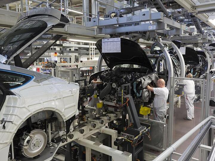 Werksmitarbeiter montieren in einer Produktionshalle von Audi bei der sogenannten "Hochzeit" den Motor an einem A6.