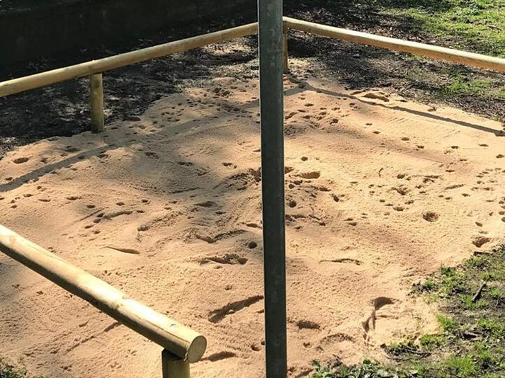 Ein Hundeklo aus Sand und abgrenzenden Holzstreben befindet sich auf einer Rasenfäche. Foto: André Winkel/Stadt Nürnberg