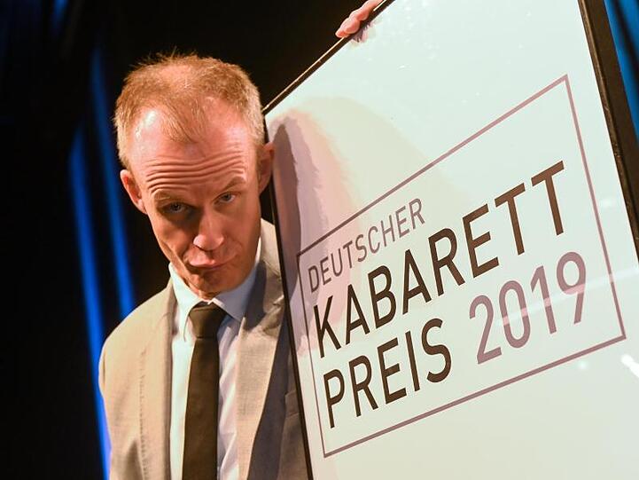 Der Münchner Kabarettist Max Uthoff steht neben einem Schild des Deutschen Kabarett-Preises. Foto: Berny Meyer/dpa