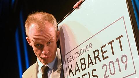 Der Münchner Kabarettist Max Uthoff steht neben einem Schild des Deutschen Kabarett-Preises. Foto: Berny Meyer/dpa