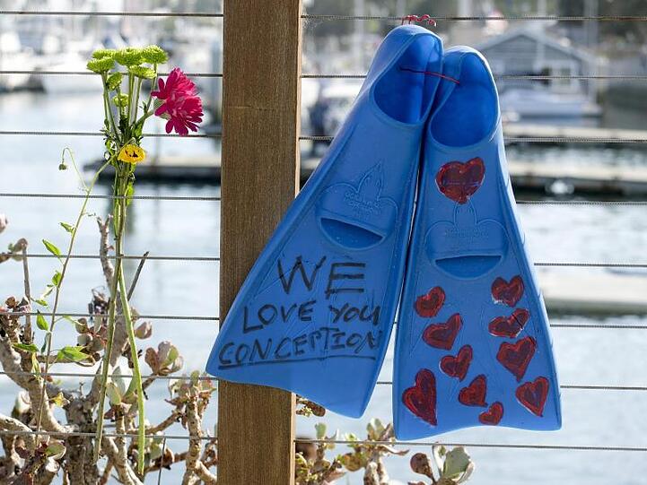 Ein Paar Flossen und Blumen hängen an einem Zaun im Hafen von Santa Barbara in Gedenken an die Opfer des Bootsfeuers.