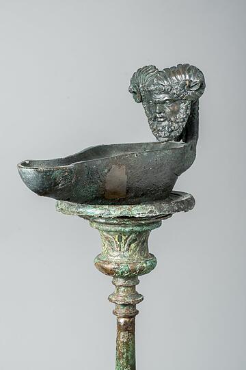 Der große Gott sieht alles: Kandelaber und Lampe mit Maske des Jupiter Ammon, aus Pompeji.