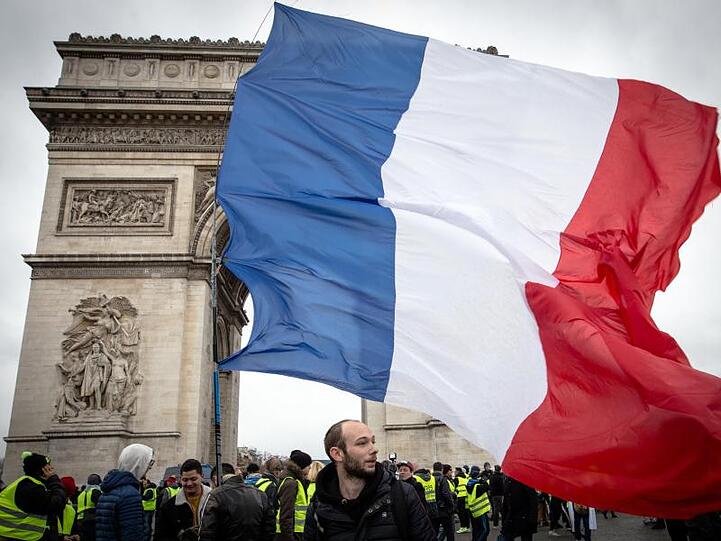 Teilnehmer einer Demonstration der "Gelbwesten" gehen mit einer französischen Nationalflagge am Arc de Triomphe in Paris entlang.
